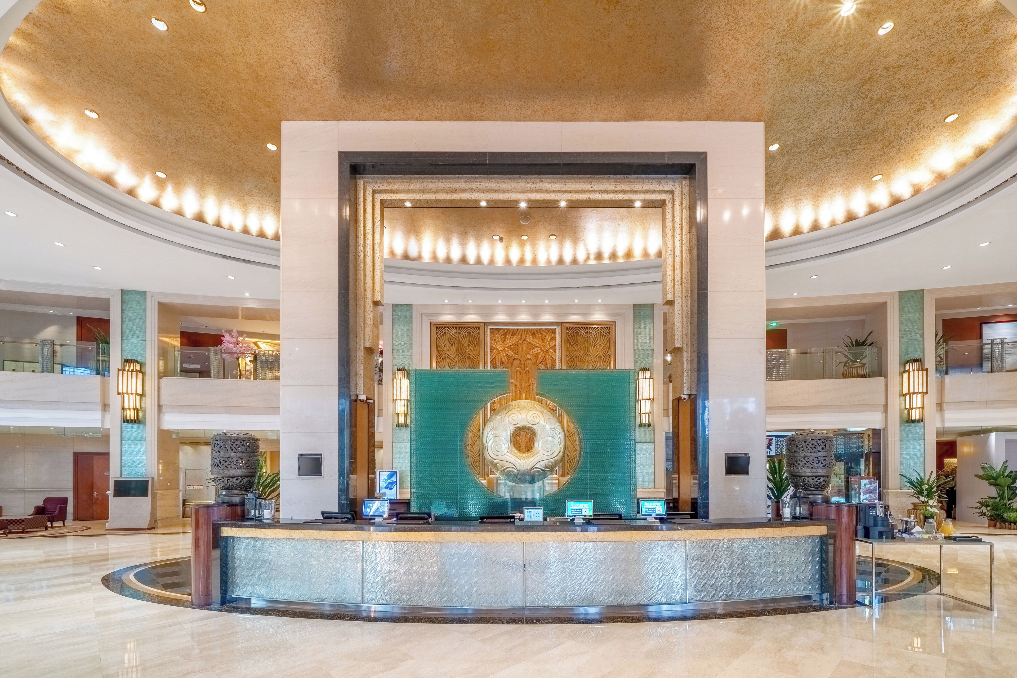 Un vestíbulo de hotel con una recepción, un gran muro decorativo y un diseño de techo circular.
