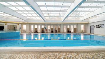 An indoor swimming pool with clear glass ceilings, multiple windows, and a tiled floor with a tactile path.