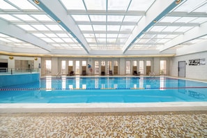 Una piscina interior con techos de vidrio transparente, múltiples ventanas y suelo de baldosas con camino accesible al tacto.