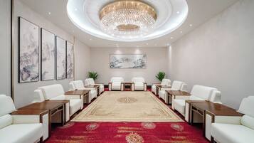 A conference room with a round table, white chairs, a red carpet, and a chandelier.