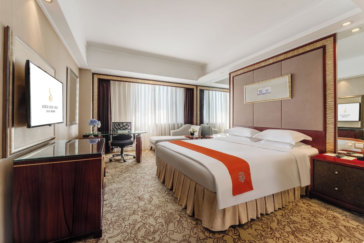 Habitación de hotel con una cama grande, un escritorio, una silla, un televisor y un minibar.