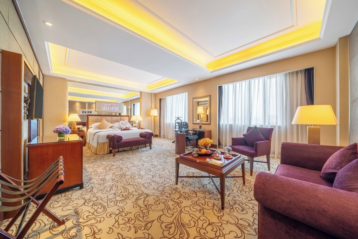 Habitación de hotel con cama, escritorio, silla, sofá y mesa de comedor con un jarrón de flores.