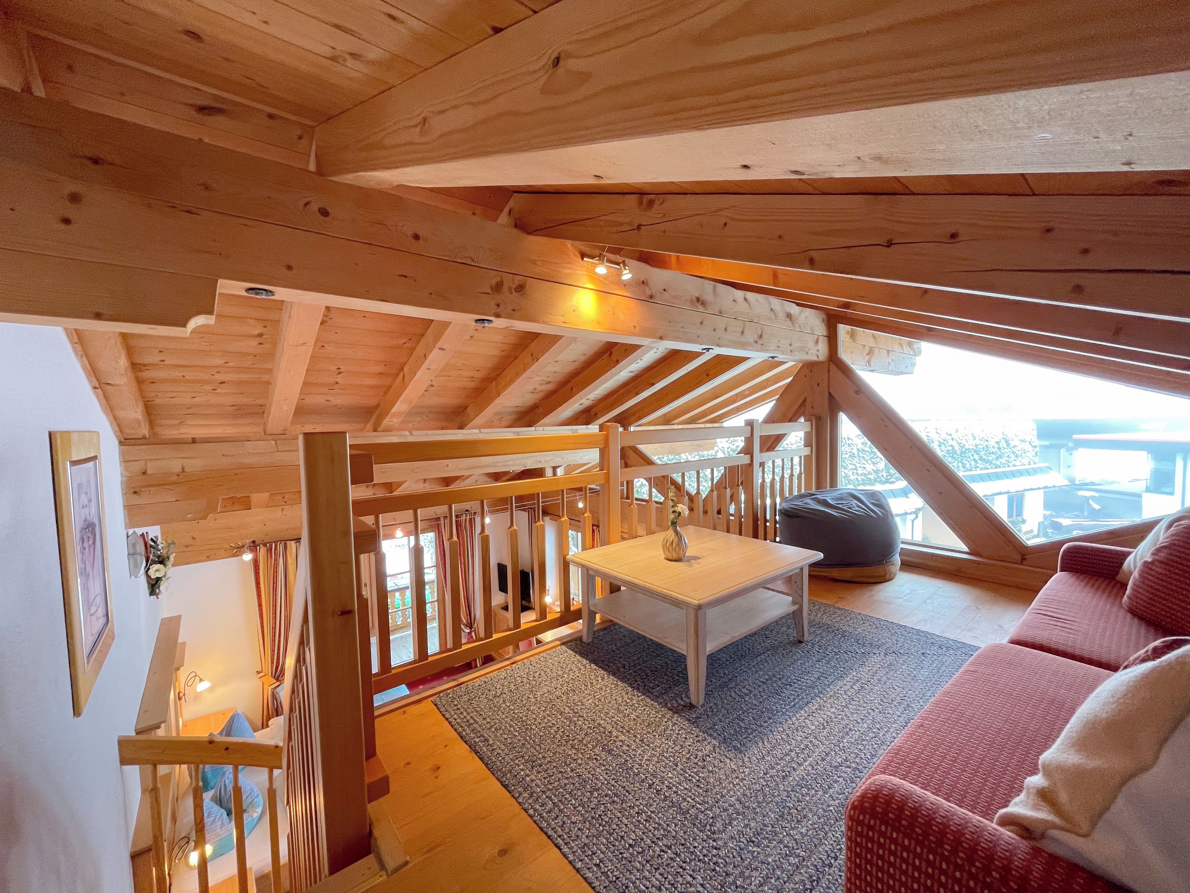 Puinen sisustus, korkea katto, valkoinen pöytä, punainen sohva ja näkymä ikkunasta.