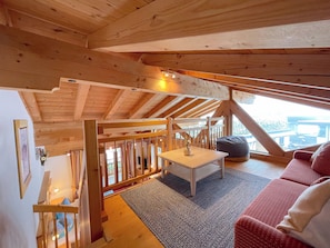 Un interior de madera con techo alto, una mesa blanca, un sofá rojo y vistas a través de una ventana.
