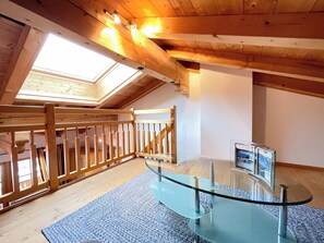Una habitación con mesa de vidrio, barandal de madera y tragaluz.