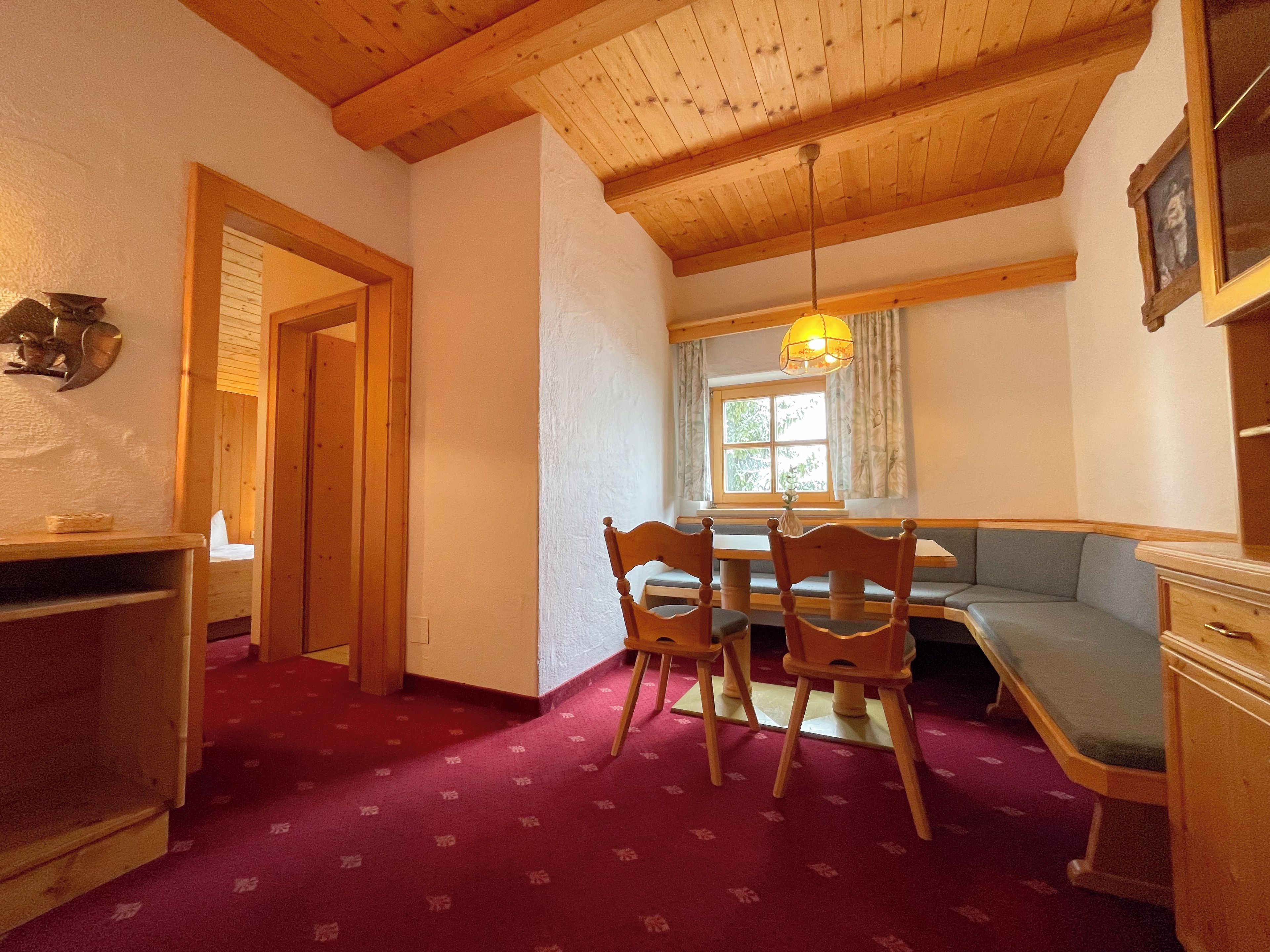 Una habitación con techo de madera, una mesa de comedor con sillas, un banco y una ventana con cortinas.
