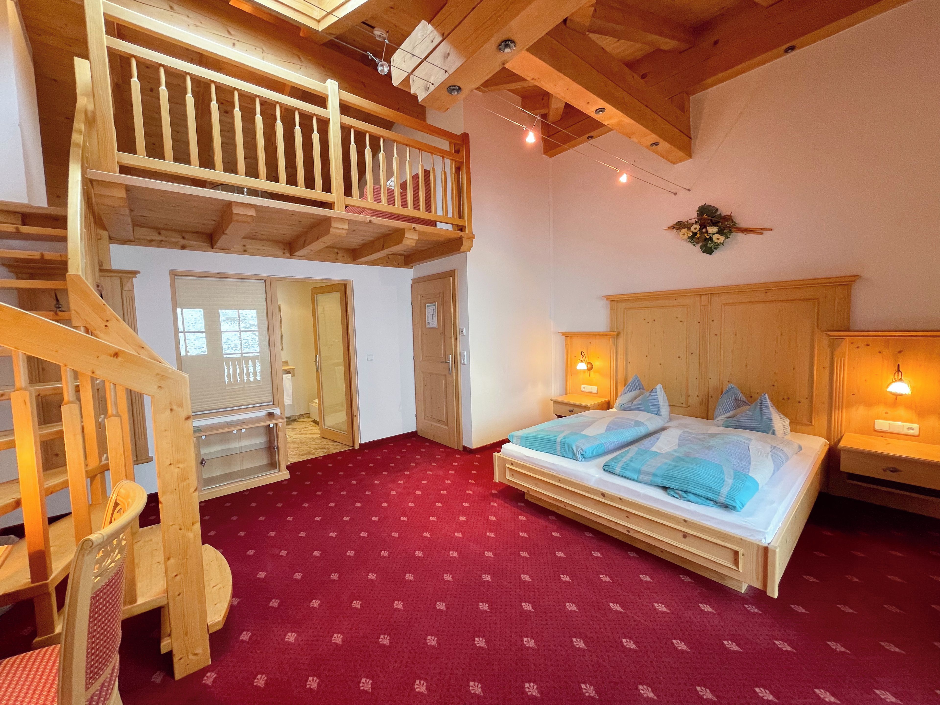 Un dormitorio con cama de madera, alfombra roja, escalera de madera y techo de madera.