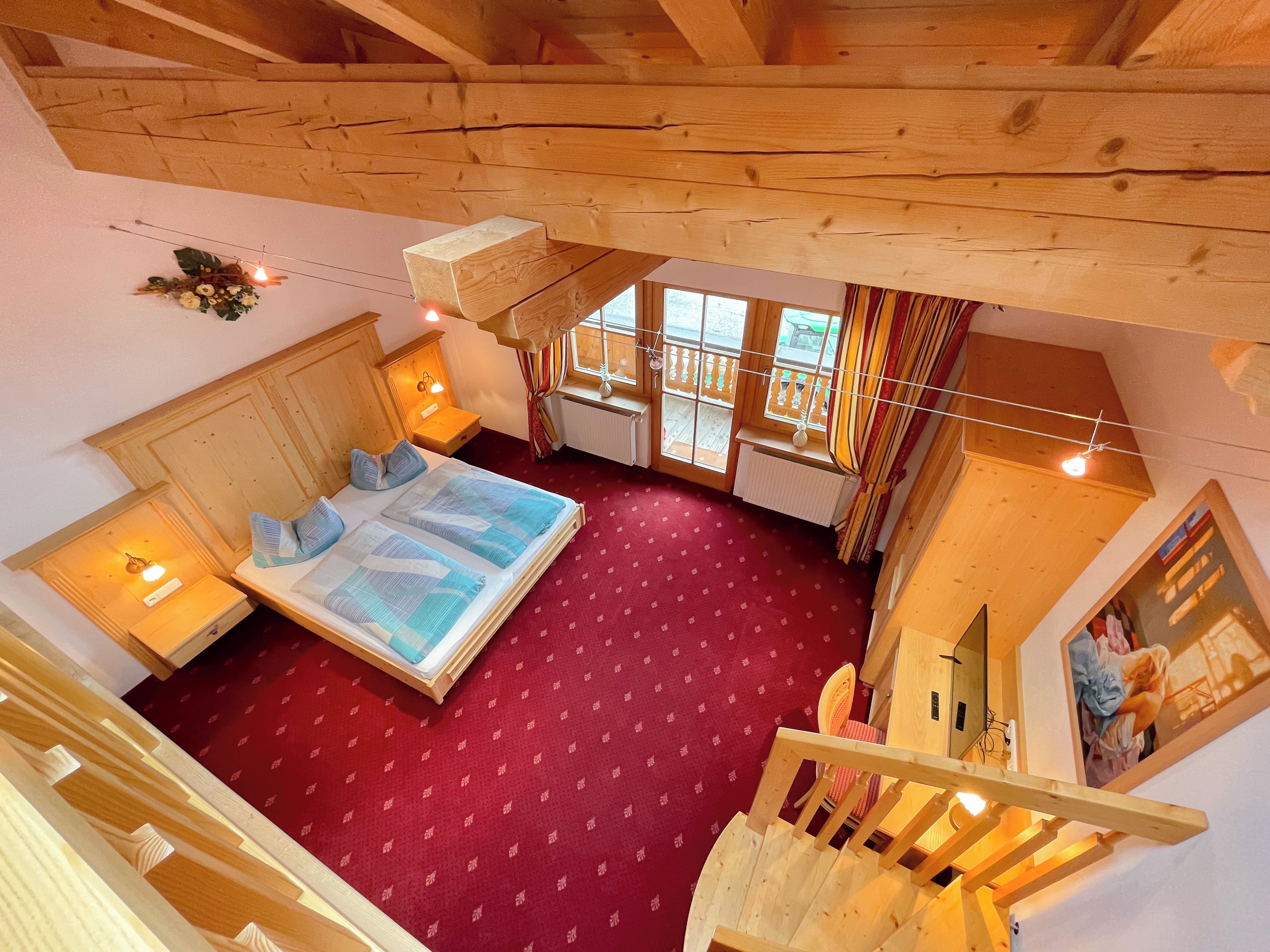 A bedroom with a large bed, wooden headboard, two bedside tables, a window with curtains, and a red carpet.
