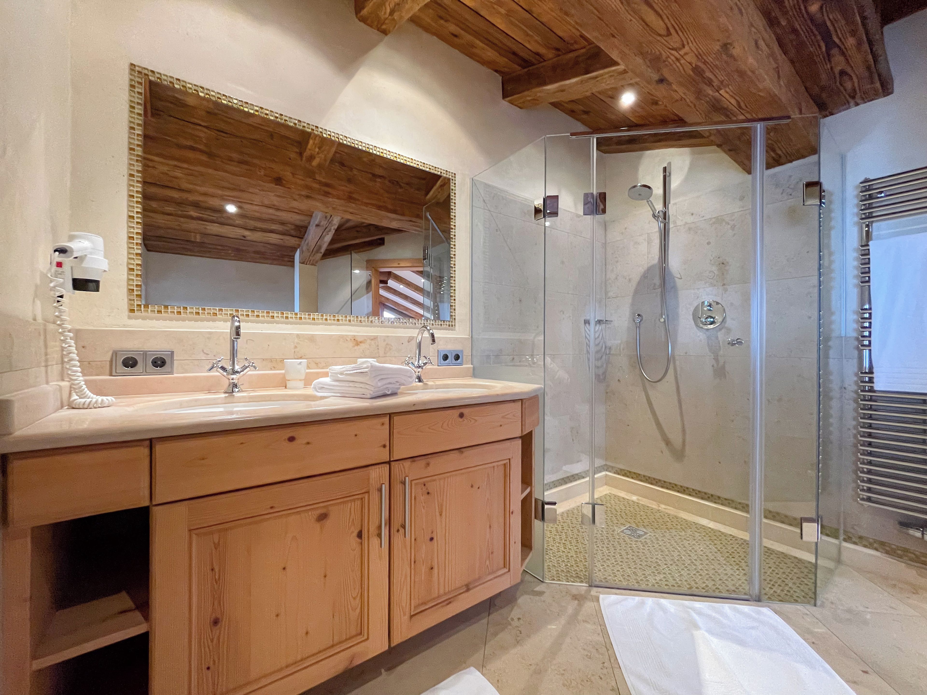 A bathroom with a wooden vanity, a large mirror, a glass-enclosed shower, and a towel rack.