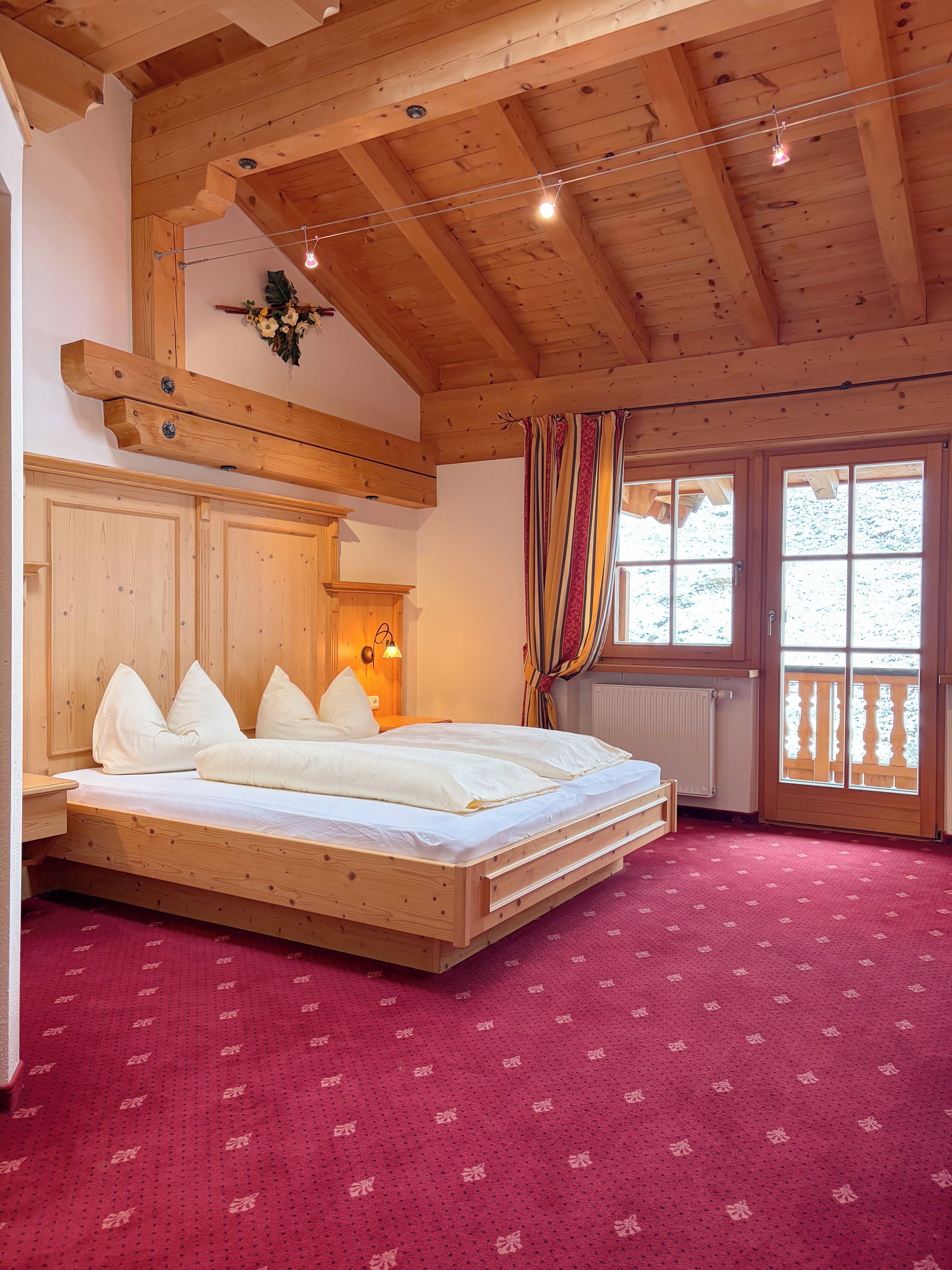 Un dormitorio con estructura de madera, una cama, una ventana con cortinas y un radiador.