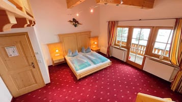 A room with a bed, wooden headboard, two bedside tables with lamps, a window with curtains, and a red carpet.