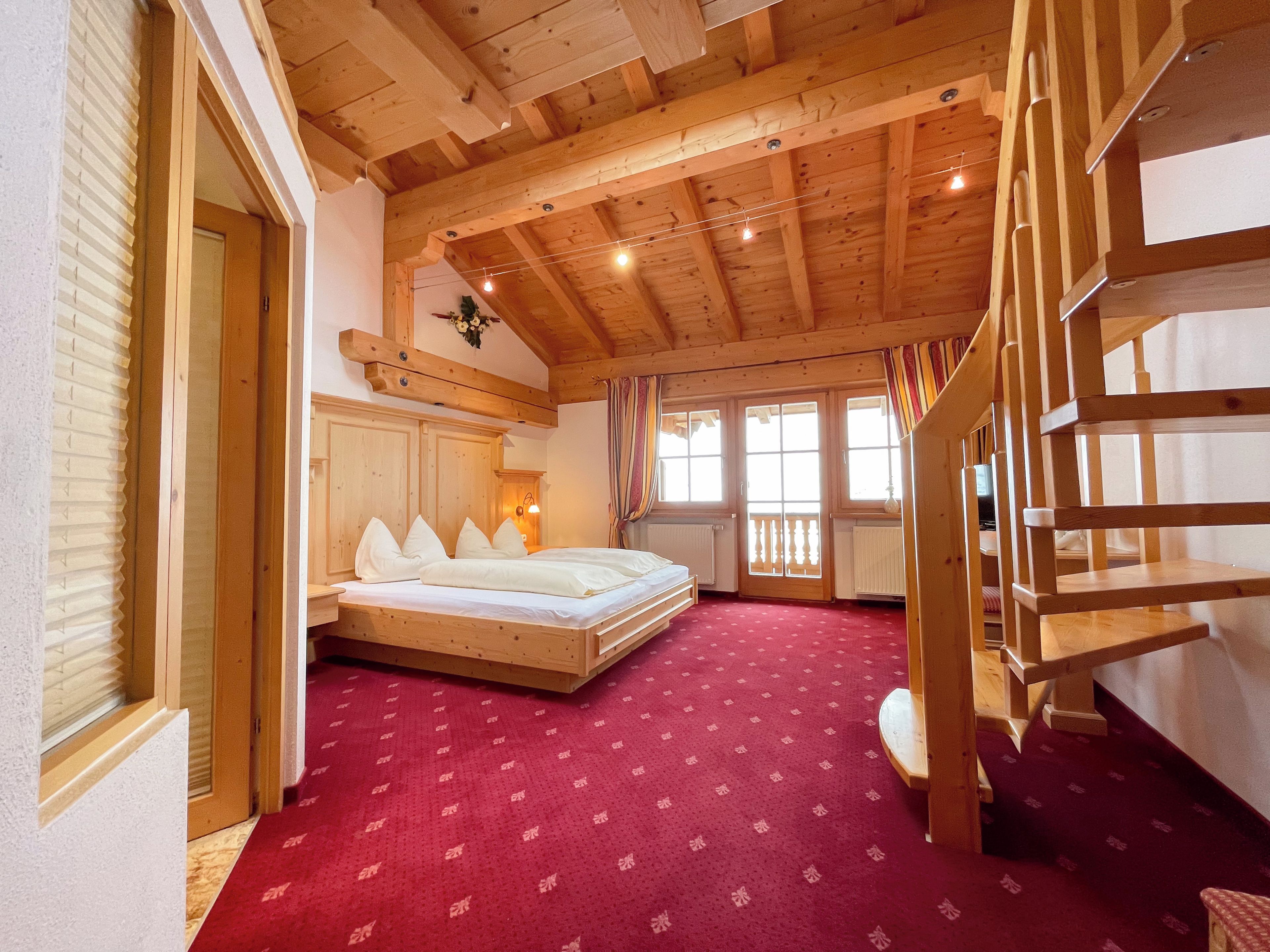 A room with a wooden ceiling, a bed with pillows, a red carpet, and a wooden staircase.