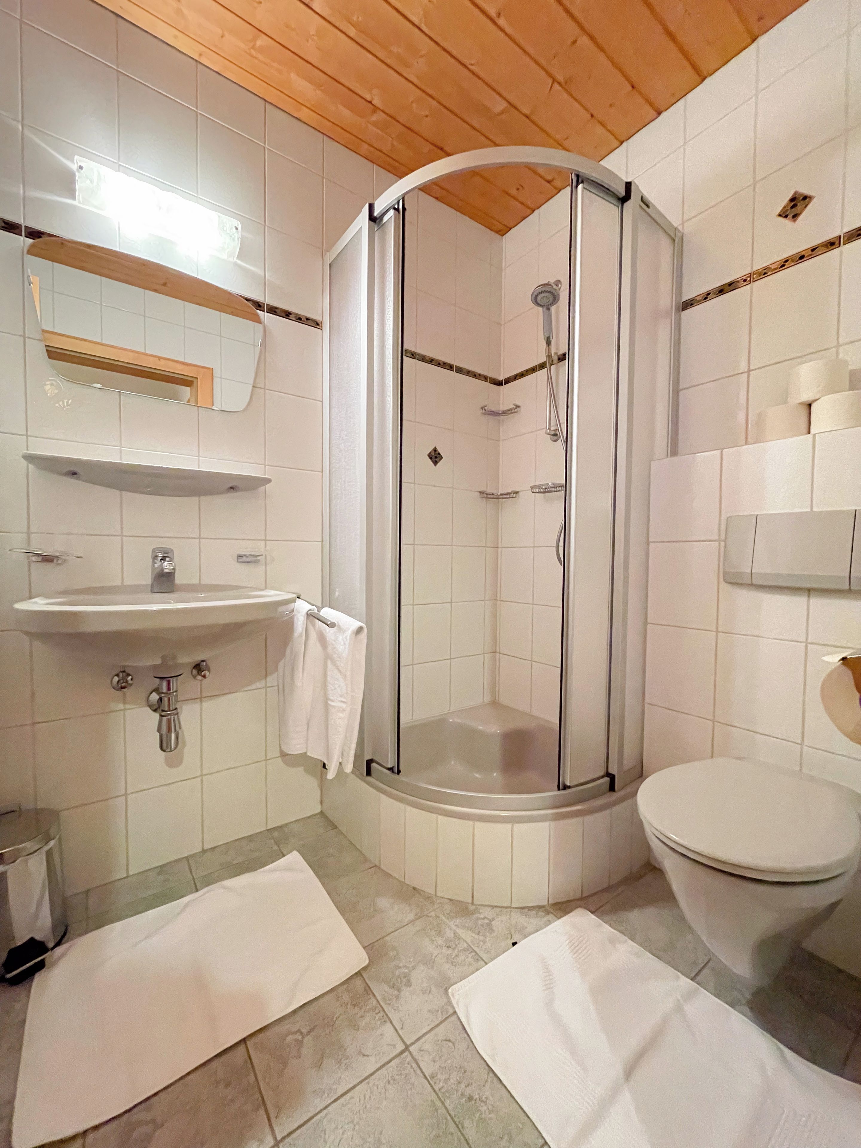Ein Badezimmer mit einer Duschkabine, einem Waschbecken, einer Toilette und zwei weißen Handtüchern auf dem Boden.