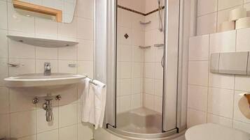 Ein Badezimmer mit einer Duschkabine, einem Waschbecken, einer Toilette und zwei weißen Handtüchern auf dem Boden.