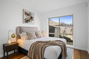 Ein Schlafzimmer mit großem Fenster, einem Bett mit Kopfteil, Nachttischen und einem gerahmten Bild an der Wand.