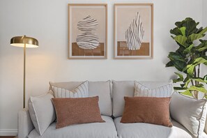 Ein Sofa mit zwei Kissen, eine Stehlampe und zwei gerahmte abstrakte Kunstwerke an der Wand.