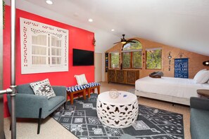 A room with a red accent wall, a white sofa, a blue sofa, a patterned rug, and a ceiling fan.