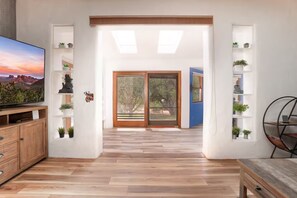 A modern living room with a wooden floor, a TV, a wooden cabinet, and a bookshelf with plants.