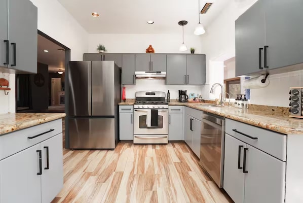 A modern kitchen with grey cabinets, stainless steel appliances, and a wooden floor.