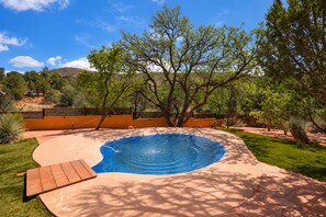 A swimming pool with a wooden deck, surrounded by a landscaped garden and a fence.