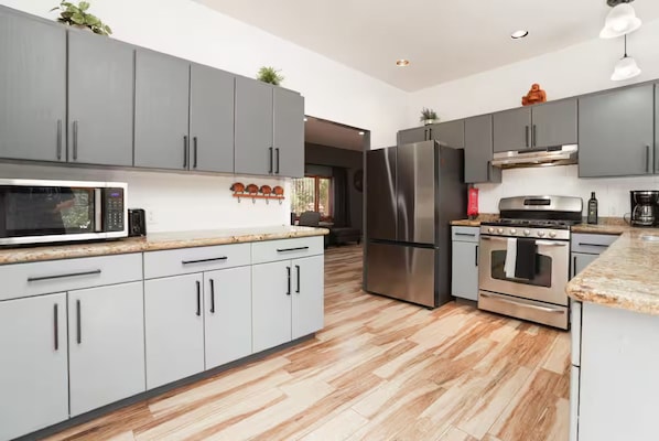 A modern kitchen with grey cabinets, stainless steel appliances, and a wooden floor.