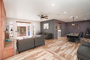 A spacious living area with a sofa set, a dining table with chairs, and a ceiling fan.