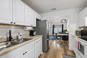 Een moderne keuken met witte kasten, roestvrijstalen apparatuur en een eethoek met een blauw vloerkleed.