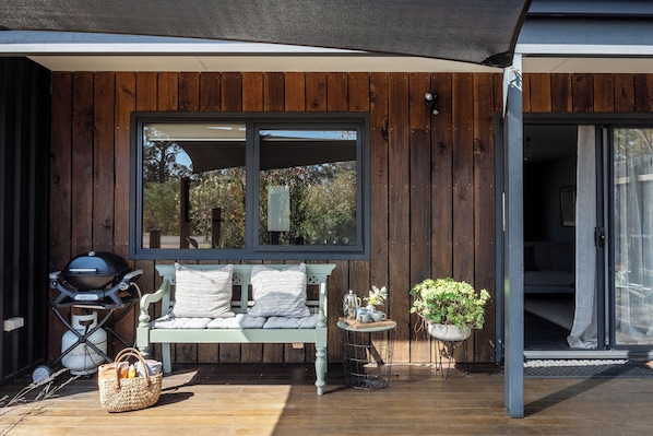 A wooden deck with a bench, a grill, and a small table with cups and a plant.