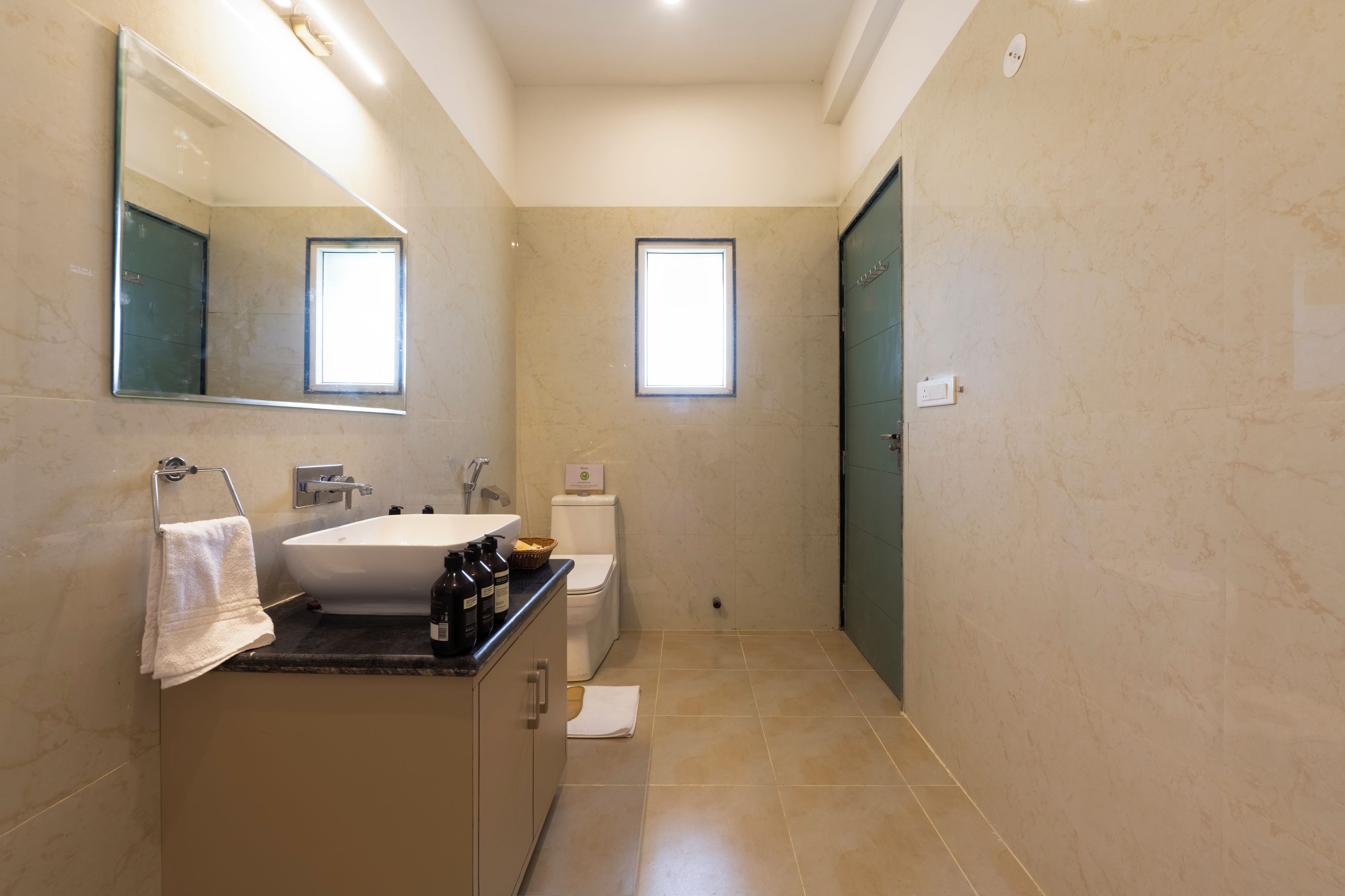 Een moderne badkamer met een ruime wastafel, spiegel en twee ramen.