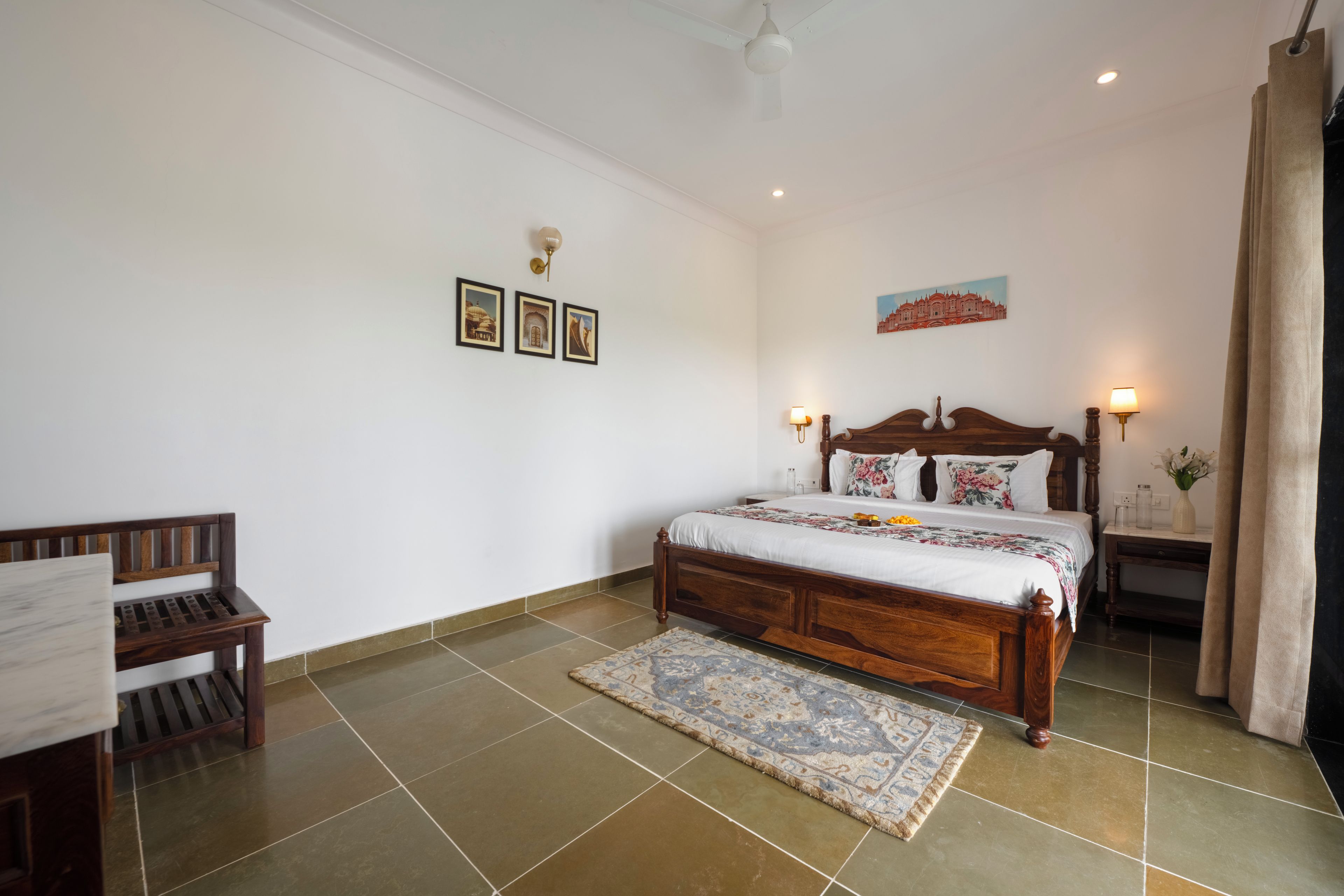 A bedroom with a wooden bed, a nightstand, a chair, a wall-mounted lamp, and a painting.