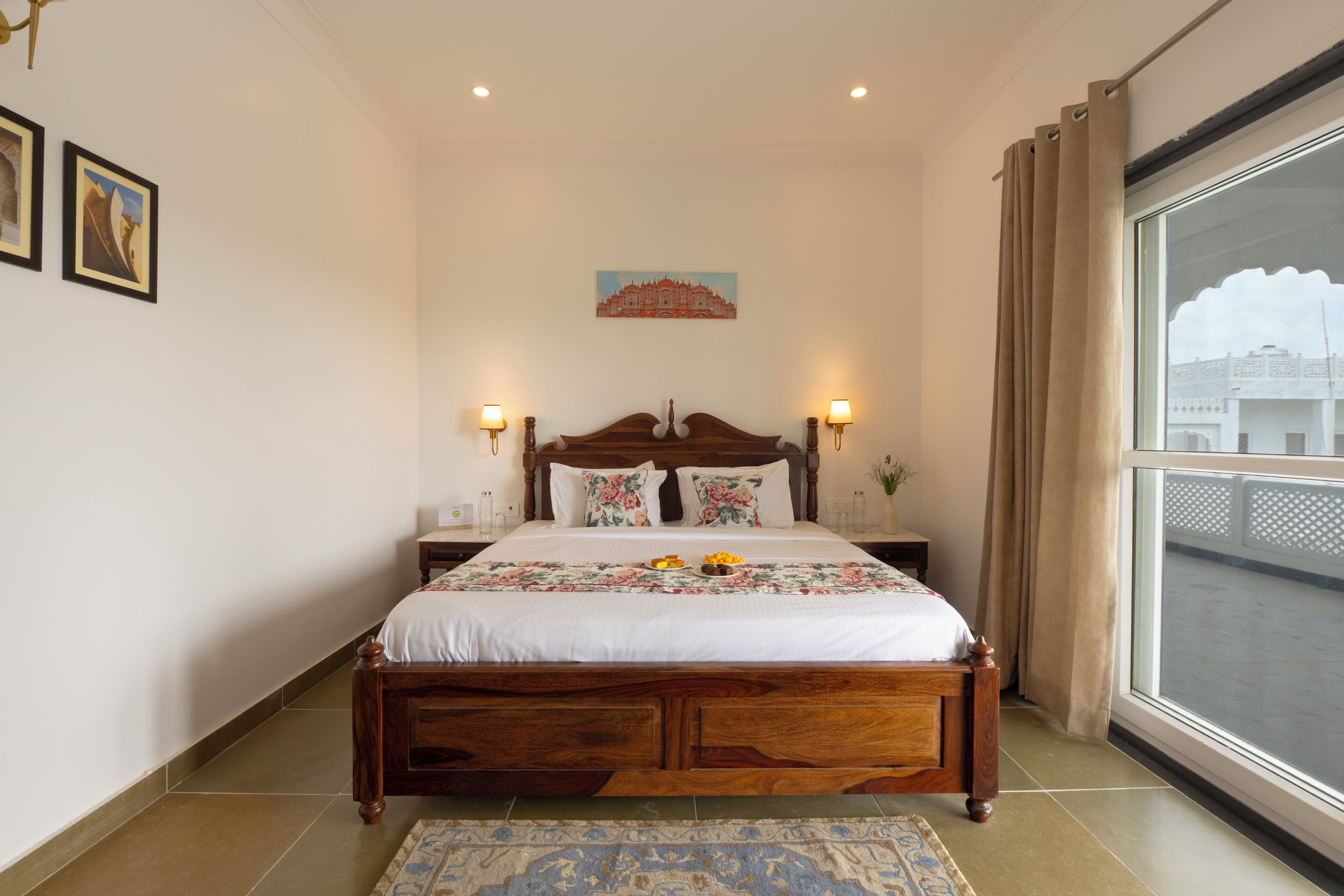 A neatly made bed with a floral bedspread, two bedside lamps, and a painting on the wall.