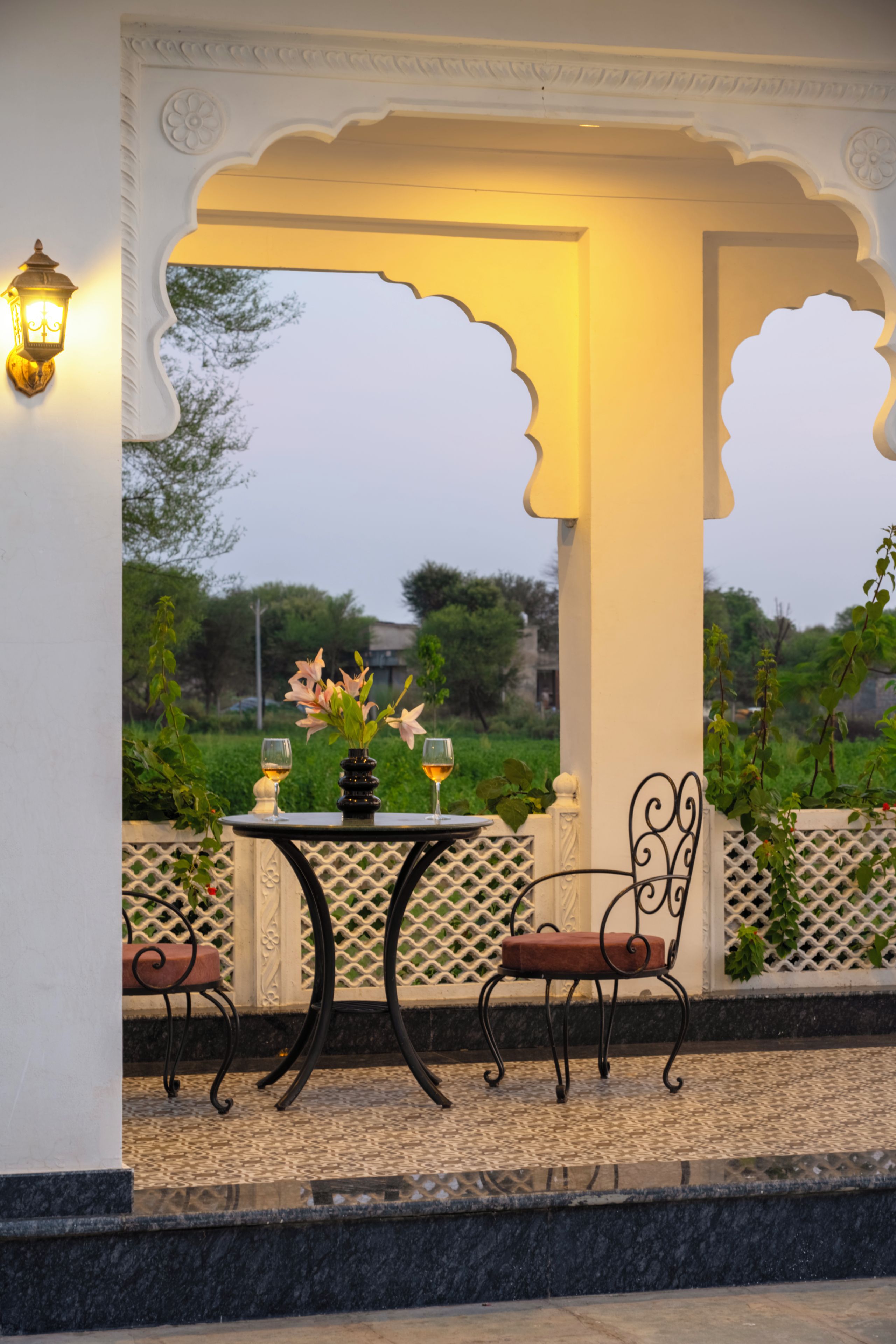 An outdoor seating area with a table and chairs, a vase with flowers, and a view of greenery.