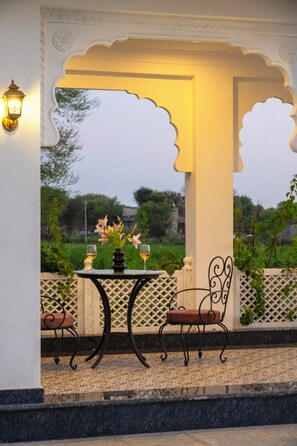 An outdoor seating area with a table and chairs, a vase with flowers, and a view of greenery. - ELIVAAS Signature Vijaypura Bagh 6BHK (Vijaipura)