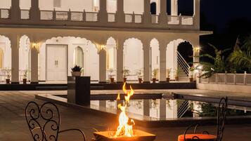A courtyard with a fire pit and two chairs, a building with multiple arches and balconies, and a staircase leading to an upper level.