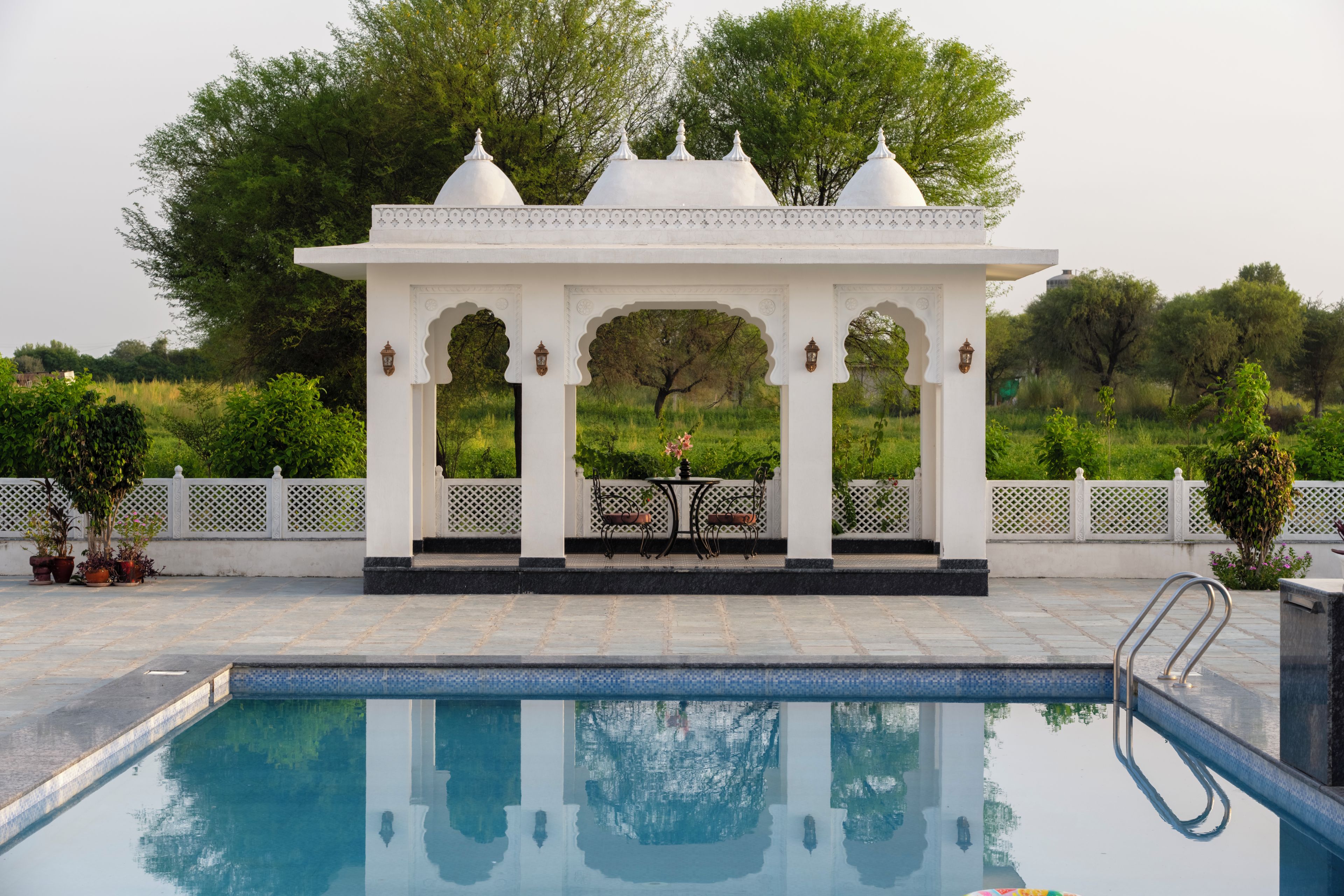 A pool area with a white gazebo structure, a table, and chairs.