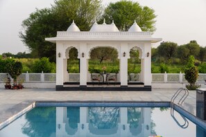 A pool area with a white gazebo structure, a table, and chairs. - ELIVAAS Signature Vijaypura Bagh 6BHK (Vijaipura)
