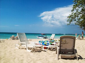 Ein Strand mit weißen Liegestühlen und einem Boot im Wasser.