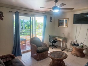 Ein Wohnzimmer mit Deckenventilator, Schreibtisch mit Stuhl, Rattan-Sofa und Glastisch.