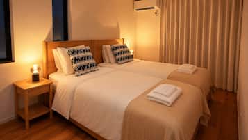 Une chambre d’hôtel avec deux lits, une table de chevet avec une lampe, une fenêtre et un appareil de climatisation.