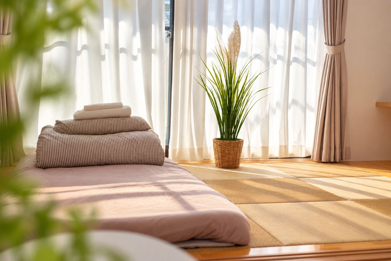 A room with a bed, a potted plant, and sheer curtains.