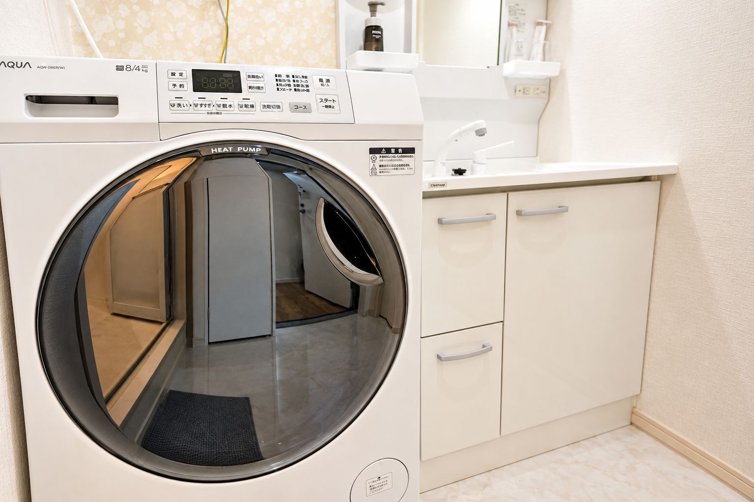 Une machine à laver à chargement frontal dotée d’un écran numérique, d’un panneau de commande et d’un sèche-linge intégré. On y trouve un plan de travail blanc, un évier et un miroir au-dessus.