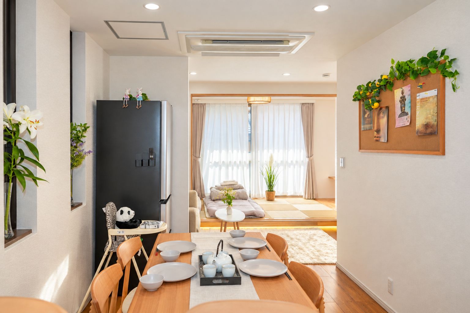 A modern dining area with a wooden table set for four, a black refrigerator, and a sofa in the background.