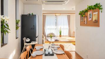 A modern dining area with a wooden table set for four, a black refrigerator, and a sofa in the background.
