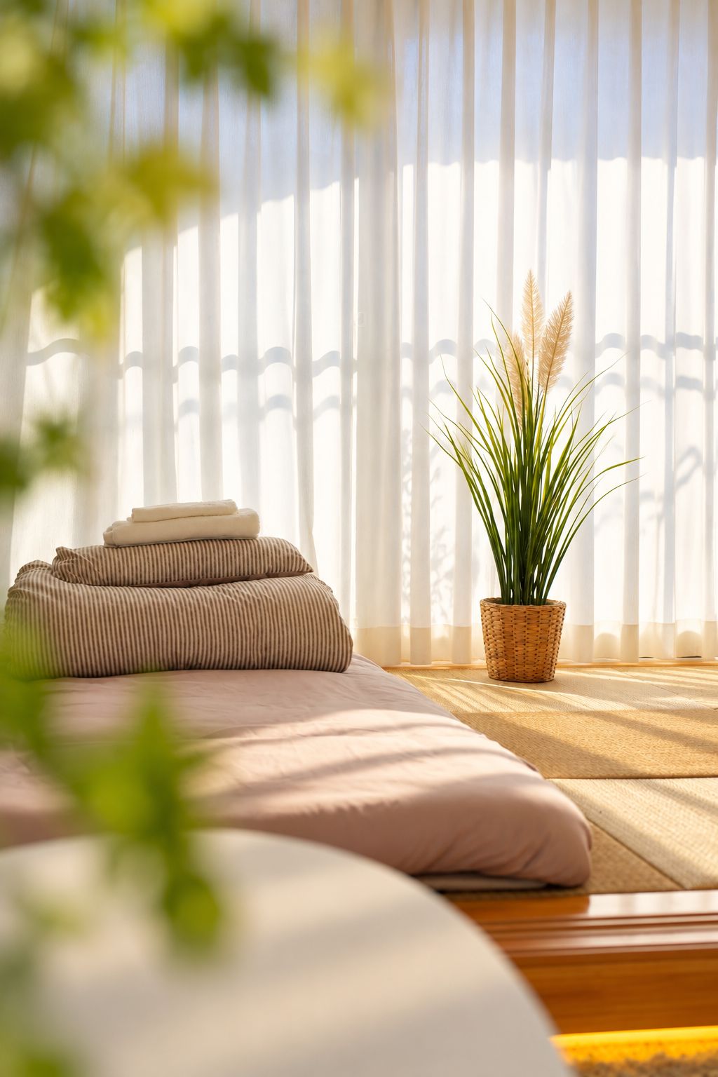 A bedroom with a bed, pillows, a potted plant, and a window with blinds.