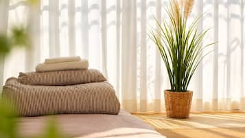 A bedroom with a bed, pillows, a potted plant, and a window with blinds.