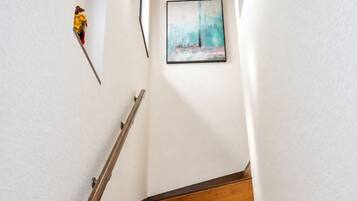 Un escalier en bois avec une rampe, des murs blancs et un tableau encadré en haut.