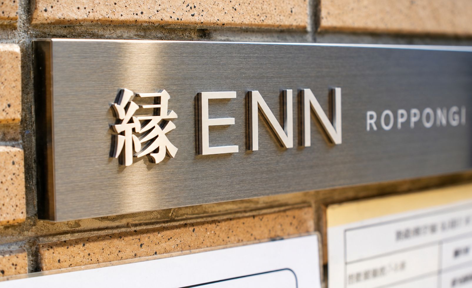 A metallic sign with 'ENN' and 'Roppongi' engraved on it, mounted on a brick wall.