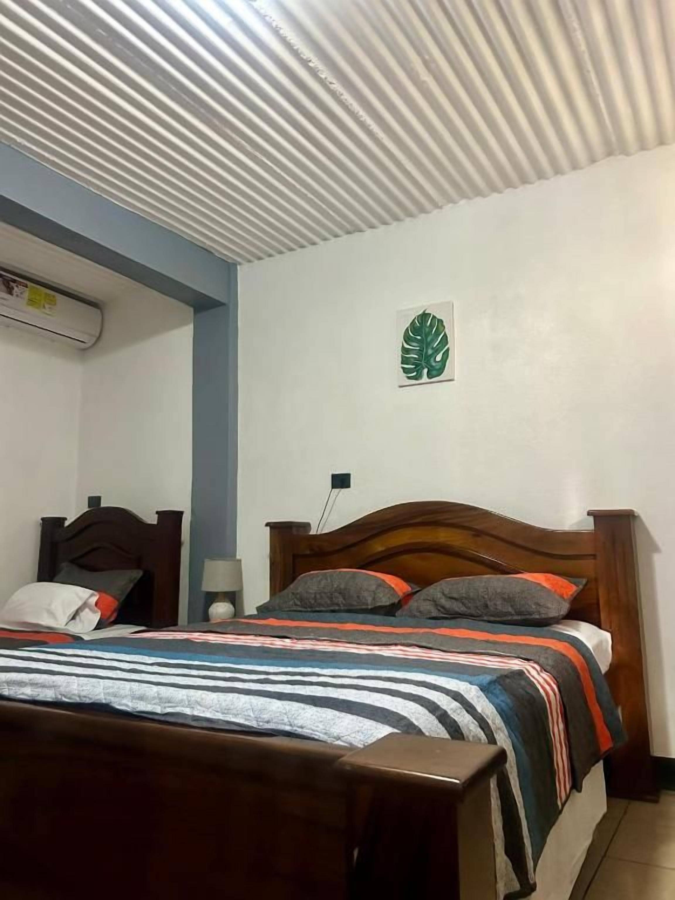 Un dormitorio con una cama de madera, un edredón a rayas, una decoración de hoja verde en la pared y un techo con diseño acanalado.