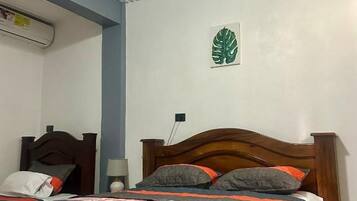 Un dormitorio con una cama de madera, un edredón a rayas, una decoración de hoja verde en la pared y un techo con diseño acanalado.
