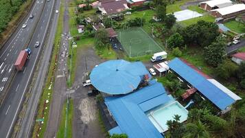 An aerial view of a residential area with a road, a large blue umbrella structure, a sports field, and several buildings.